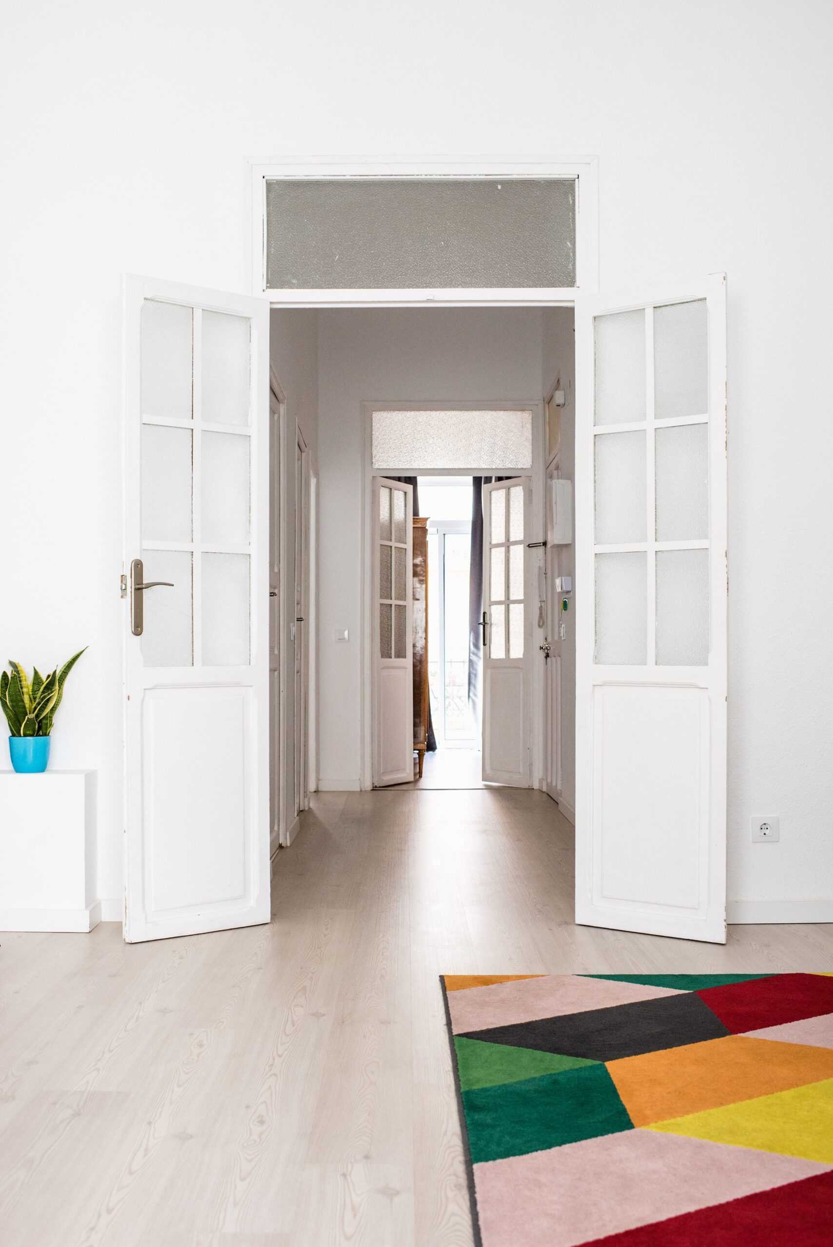 Bright minimalist hallway with open white doors and colorful geometric rug