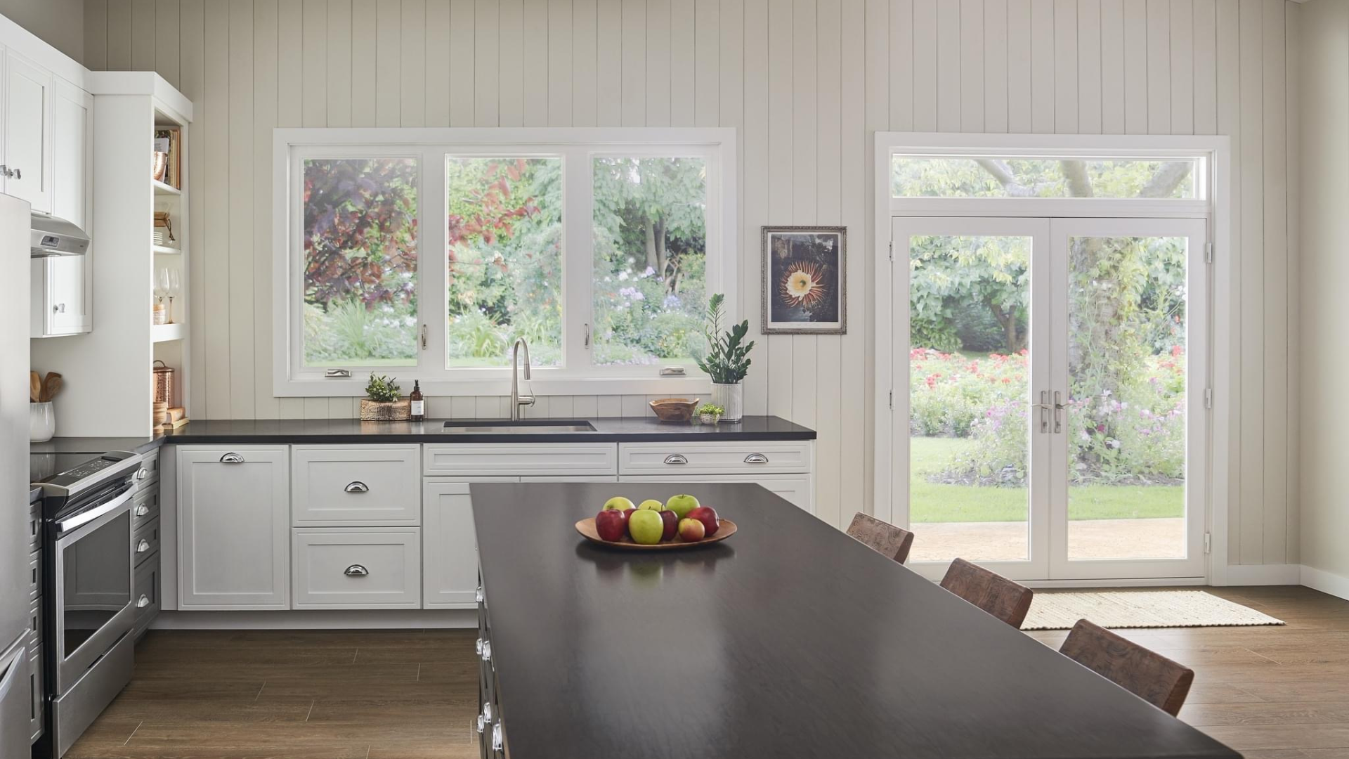 Modern white kitchen with dark island overlooking garden through large windows