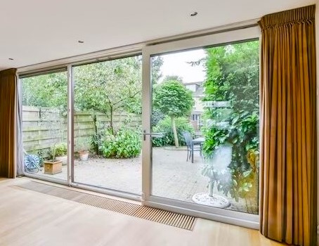 Modern living room with floor-to-ceiling glass doors opening to a garden patio with gold curtains